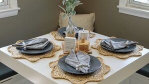 Une table à manger dressée avec des assiettes, des serviettes et des bougies, entourée de chaises blanches.