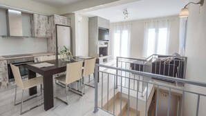 A modern kitchen with a dining area, a balcony with a railing, and a staircase leading to an upper floor.