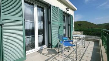 A balcony with a blue chair and a small table, a sliding glass door, and a view of green hills.
