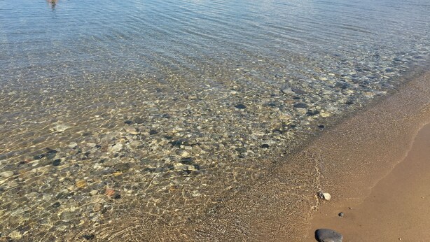 A beach with clear shallow waters revealing pebbles and a person swimming. - Sugarloaf Golf & Beach Retreat: Quiet Nature Edition (Cedar)