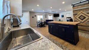 A modern kitchen with a stainless steel sink, wooden countertop, and a dining area with a table and chairs. - Sugarloaf Golf & Beach Retreat: Quiet Nature Edition (Cedar)