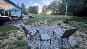 An outdoor seating area with chairs and a table, surrounded by gravel and greenery, with a building and trees in the background. - Sugarloaf Golf & Beach Retreat: Quiet Nature Edition (Cedar)
