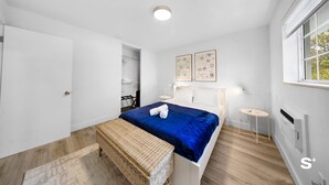 Une chambre à coucher moderne avec un lit, un banc, une petite table et des œuvres d’art accrochées au mur.