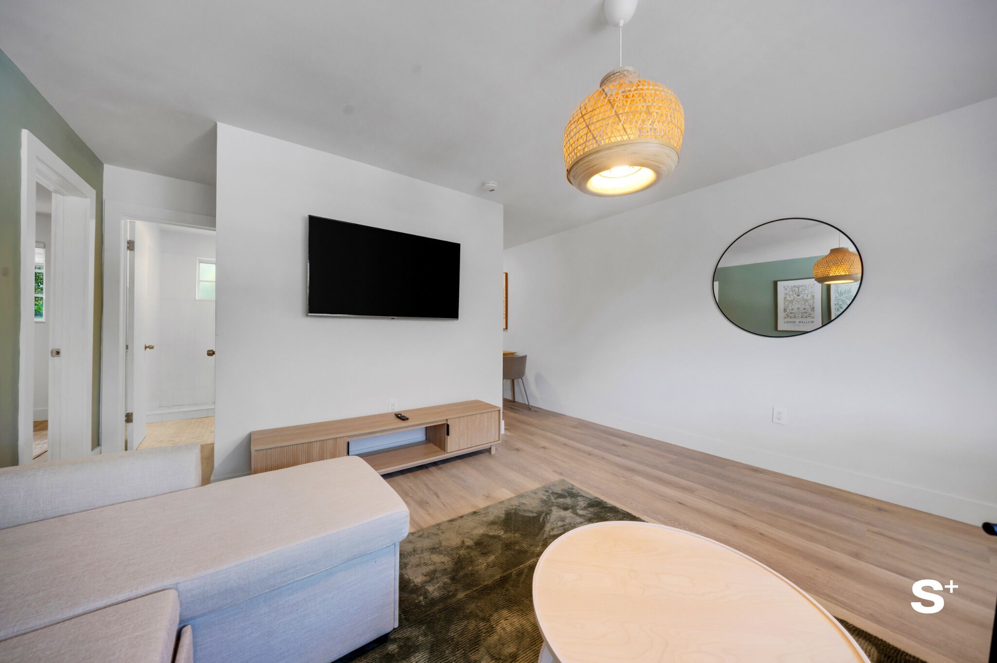 Un salon moderne doté d’un téléviseur à écran plat, d’un miroir rond et d’un luminaire tressé.