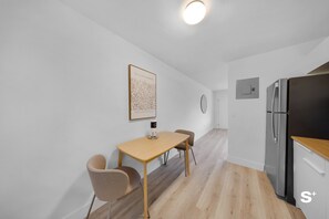 A modern kitchen with a stainless steel refrigerator, a wooden table with two chairs, and a framed artwork on the wall. - Stylish 1-BD Apt - Gym - Free Parking (North Miami)