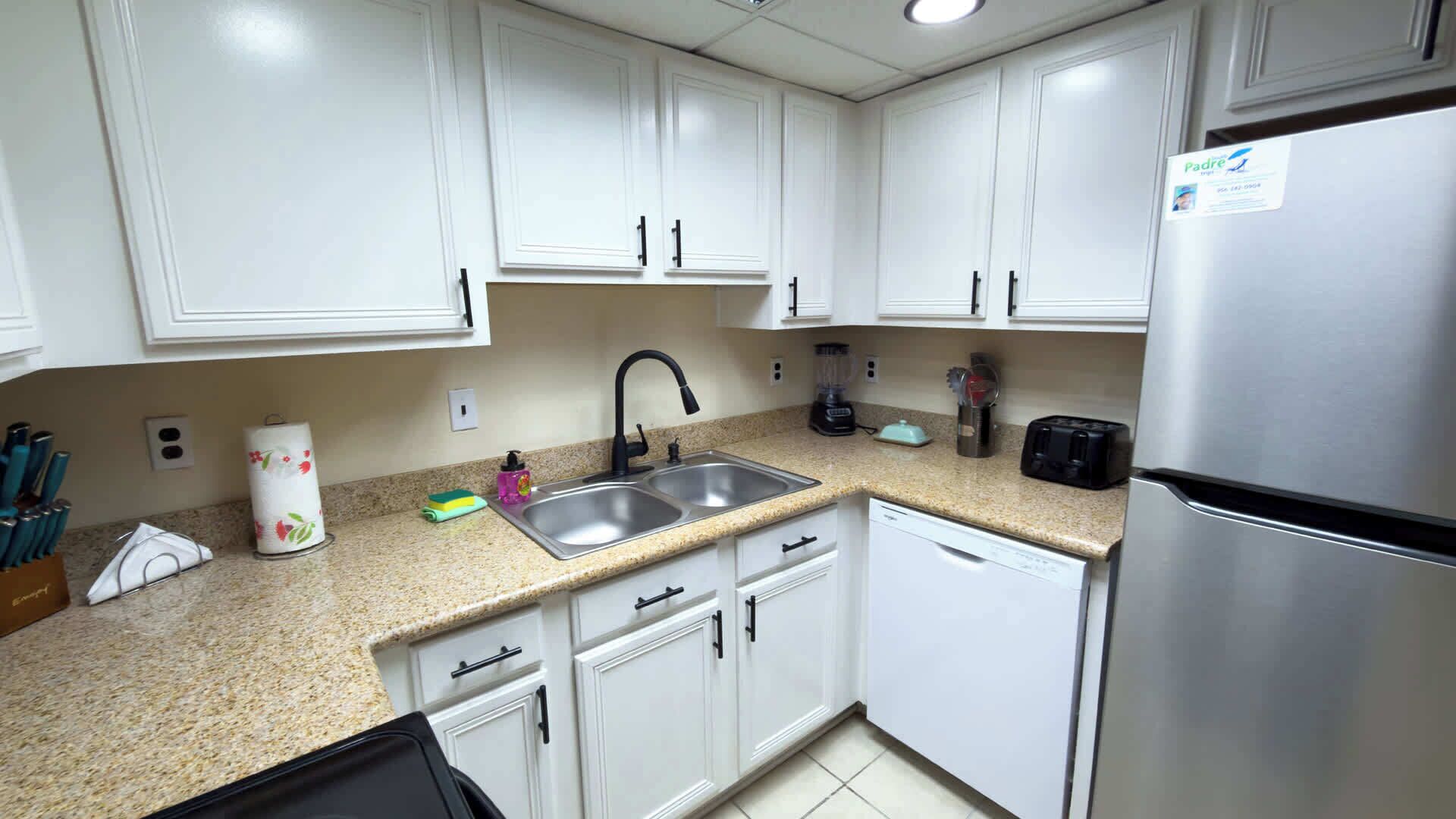 A kitchen with white cabinets, a stainless steel sink, a toaster, and a blender.