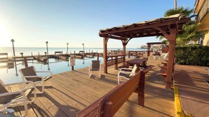 A wooden deck with lounge chairs and a pool, a wooden pergola, and a view of the ocean. - Direct Bayfront Sunsets - Boat Docks - Pool - Fish (South Padre Island)