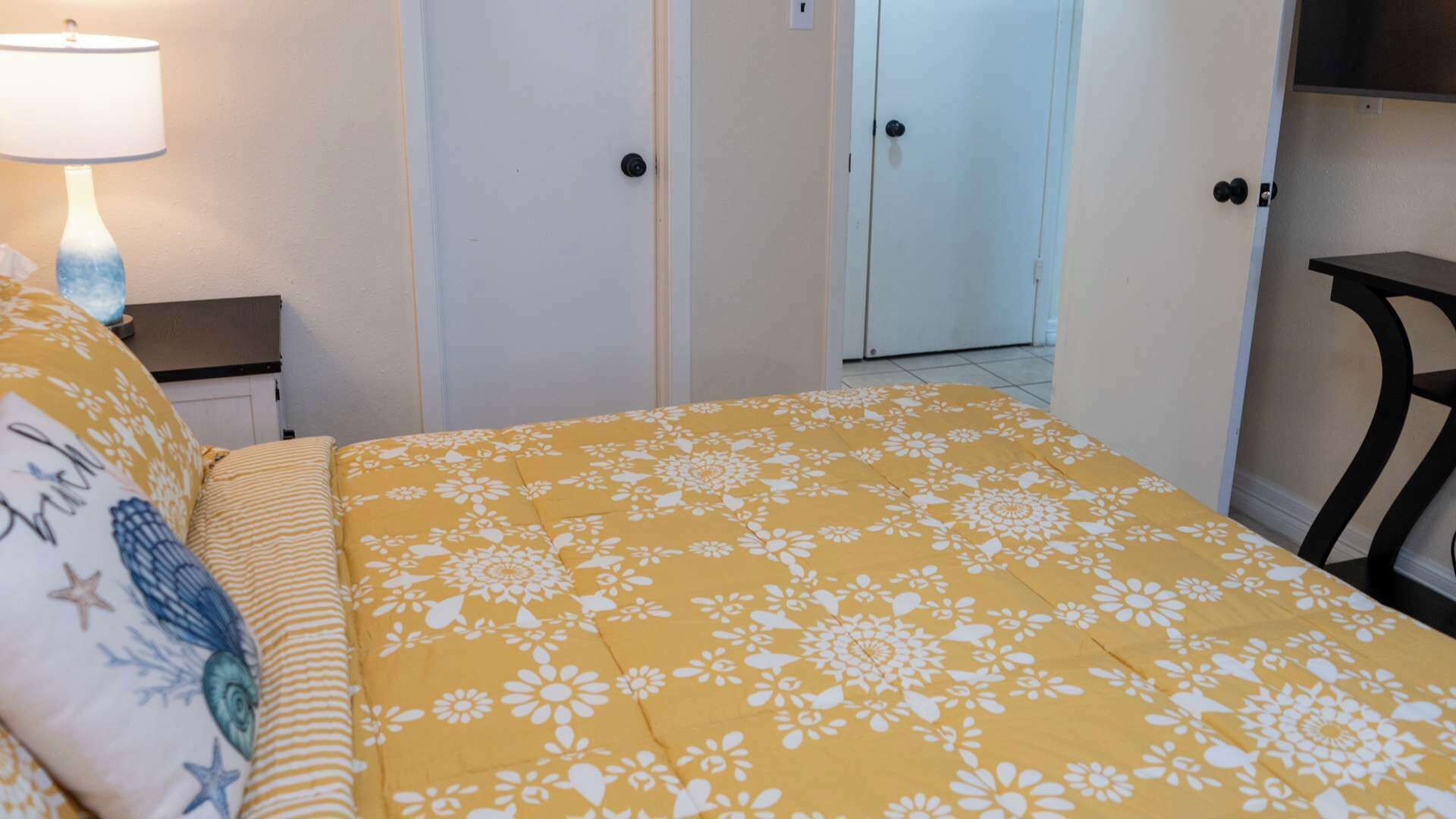 Een slaapkamer met een bed, een nachtkastje, een lamp en een deur naar een andere kamer.