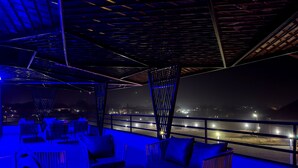 A rooftop bar with wicker furniture and a view of a cityscape at night. - PEREGRINE HOTEL BY BOULEVARD (Jos)