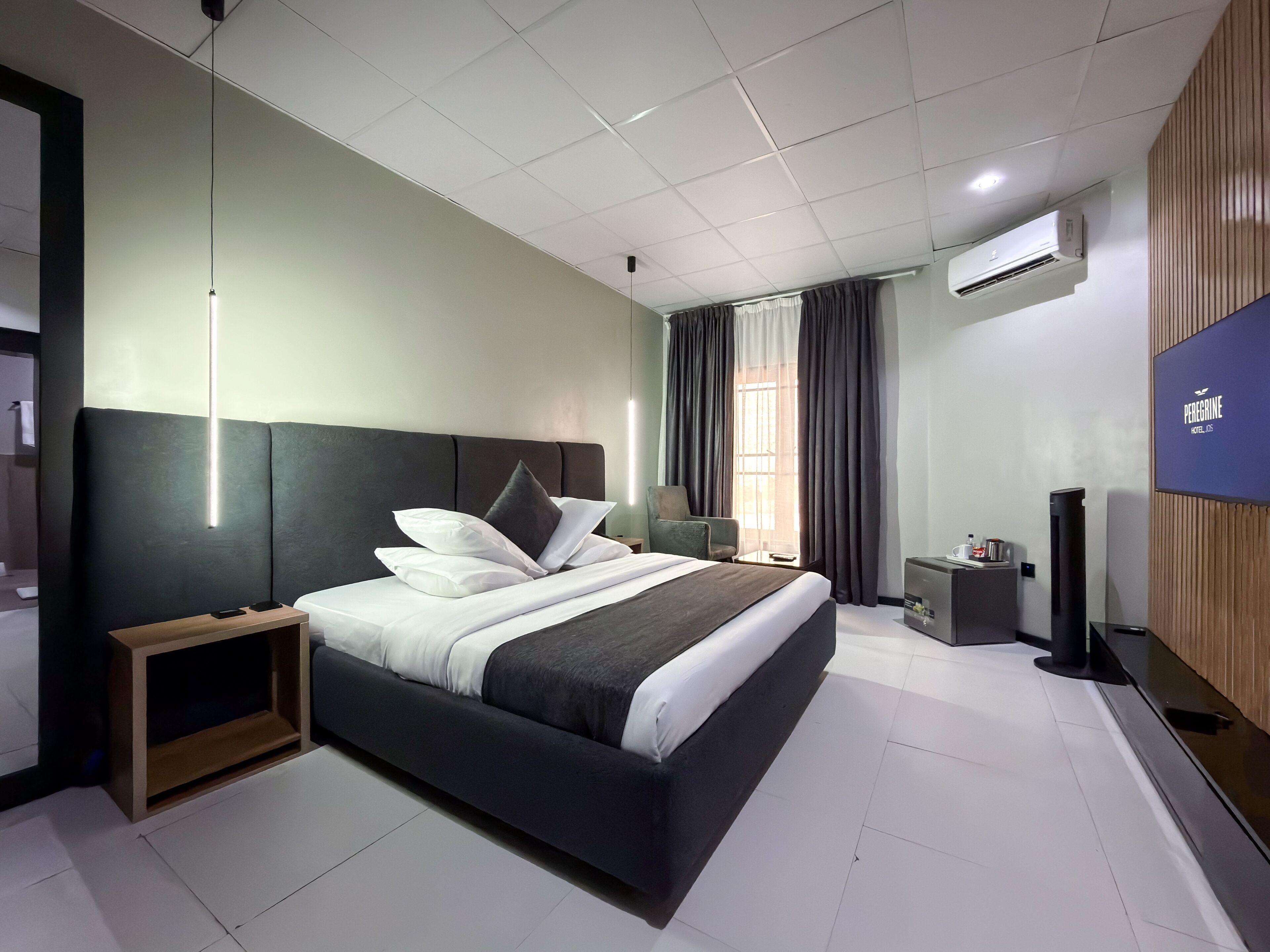 A modern hotel room with a large bed, a bedside table, a TV, and a window with curtains.
