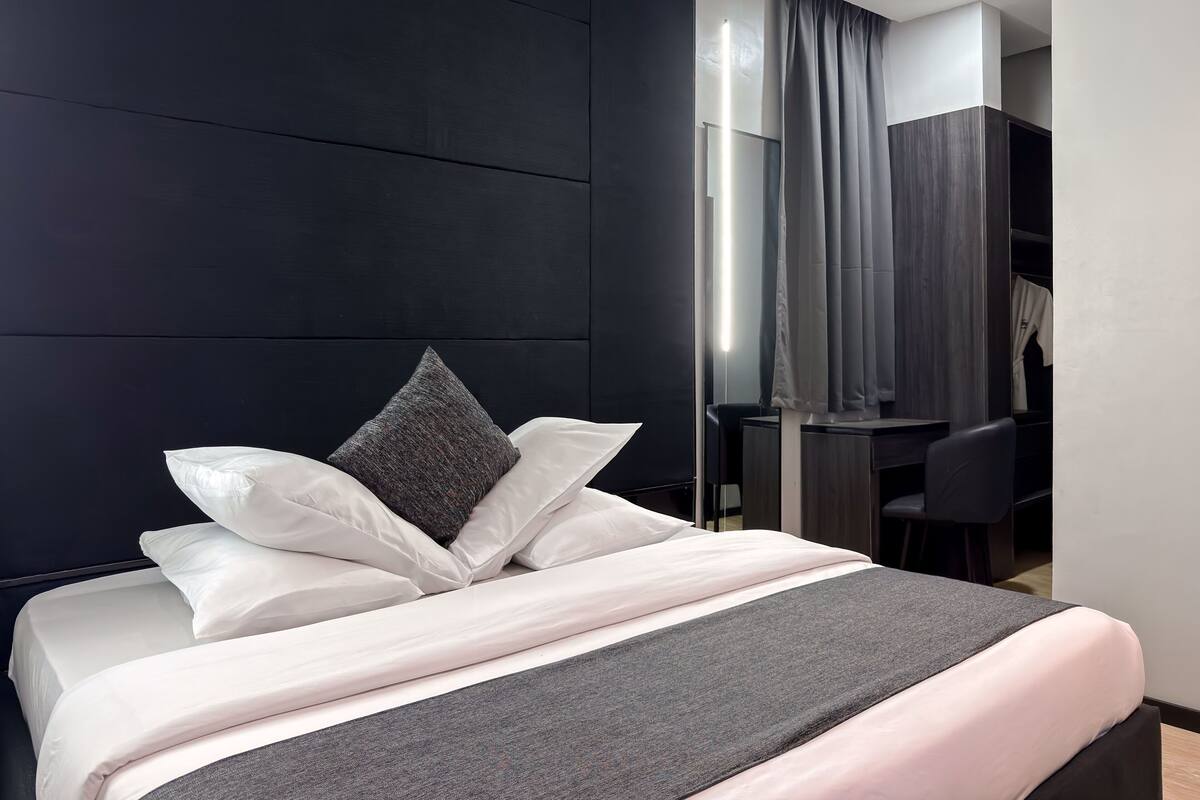 A modern hotel room with a large bed, dark wall paneling, a desk, and a chair.