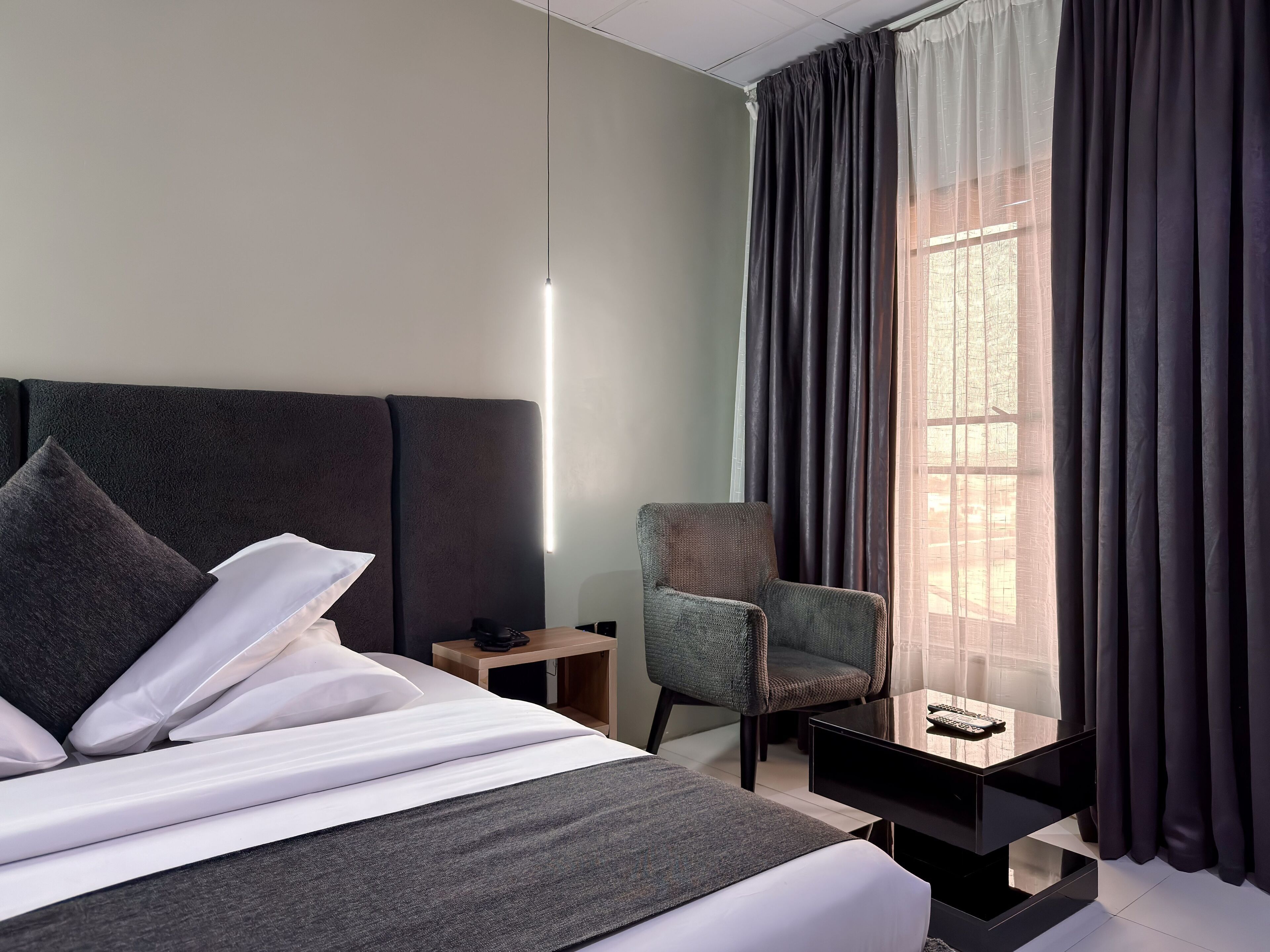 A modern hotel room with a large bed, a chair, a small table, and a window with curtains.