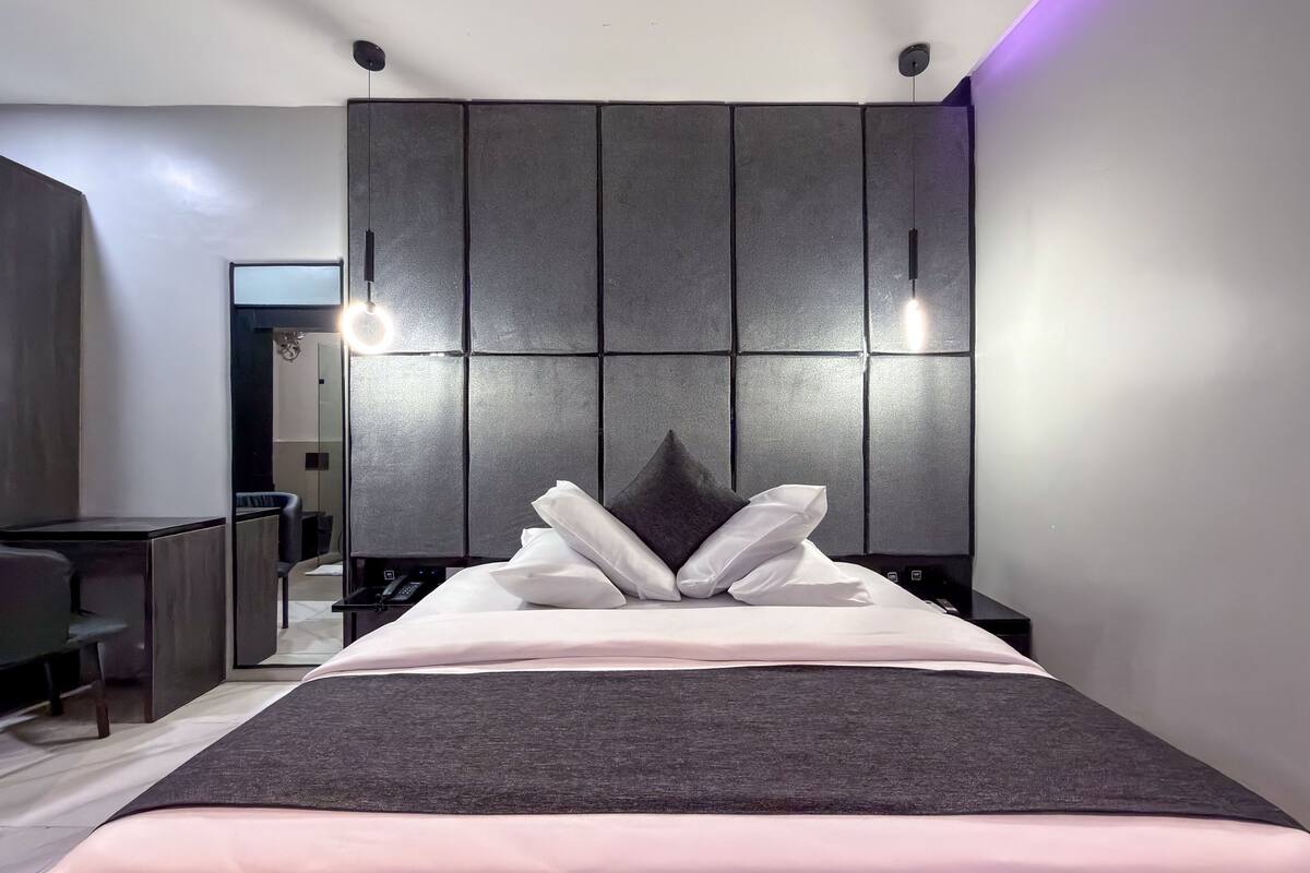 A modern bedroom with a large bed, a headboard with built-in lighting, and a desk with a chair.