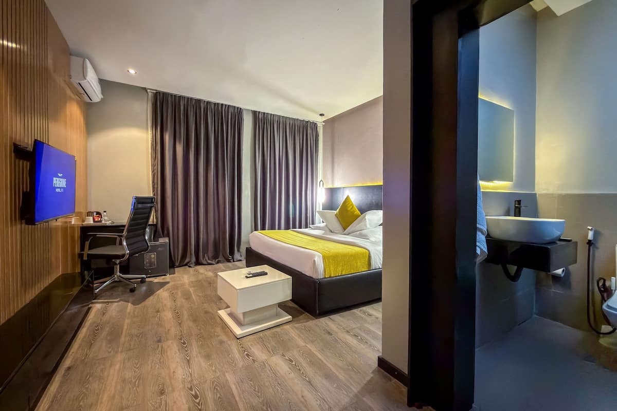 A modern hotel room with a bed, a desk, a chair, a TV, and a bathroom.