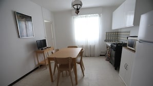 A kitchen with a dining table, chairs, a TV, and a refrigerator.