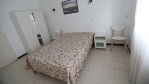 A bedroom with a bed, a wardrobe, a chair, a desk, and a wall-mounted picture.
