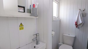A bathroom with a toilet, sink, and a caution sign for hot water. - The Comfort Den (Aberystwyth)