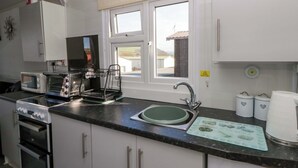 A kitchen with a sink, a microwave, a toaster, and a window with a view of buildings. - The Comfort Den (Aberystwyth)