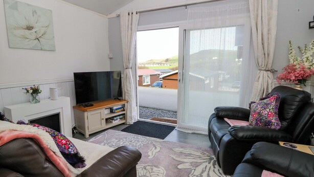A living room with a television, sofa, and a view of the outside. - The Comfort Den (Aberystwyth)