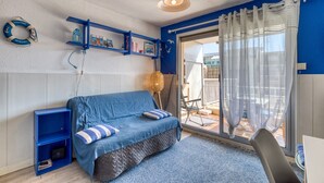 A room with a blue sofa, a small bookshelf, a lamp, and a view through a glass door to an outdoor area.