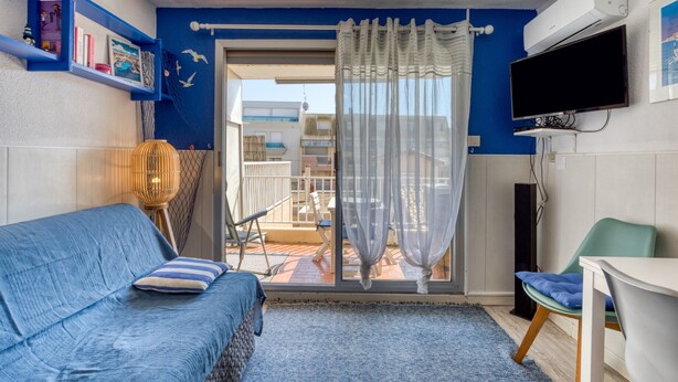 A room with a blue sofa, a chair, a TV, and a balcony with a view.