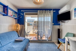 A room with a blue sofa, a chair, a TV, and a balcony with a view. - Air-conditioned Studio with Terrace (Sète)