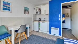 A compact room with a kitchenette, a desk, a chair, and a bed.
