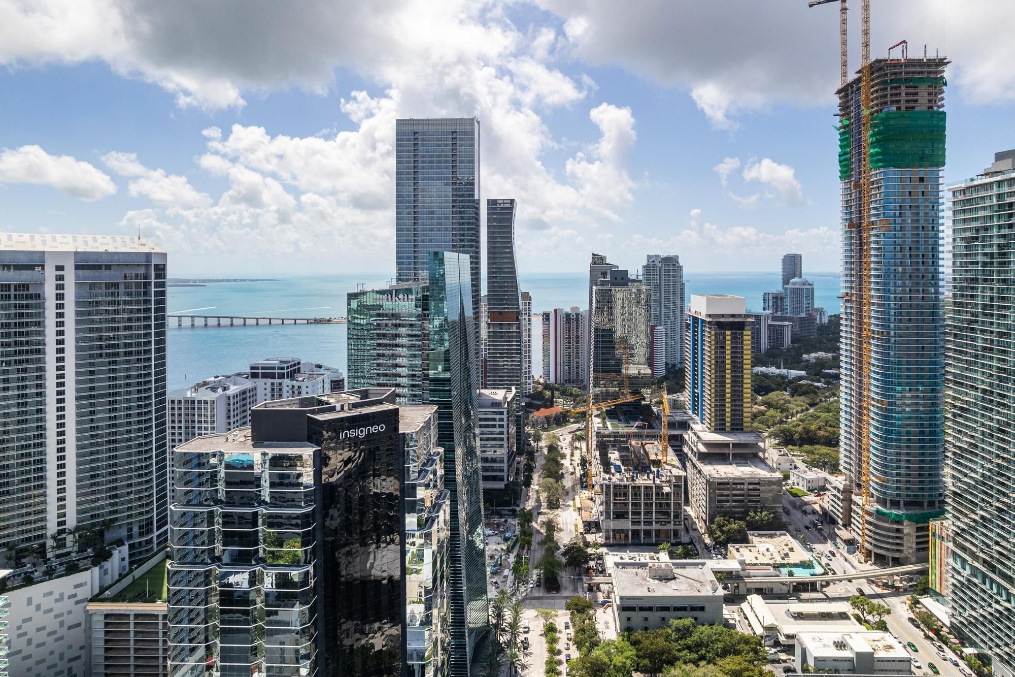 A high-rise urban area with modern skyscrapers, a bridge in the background, and a clear view of the sea.