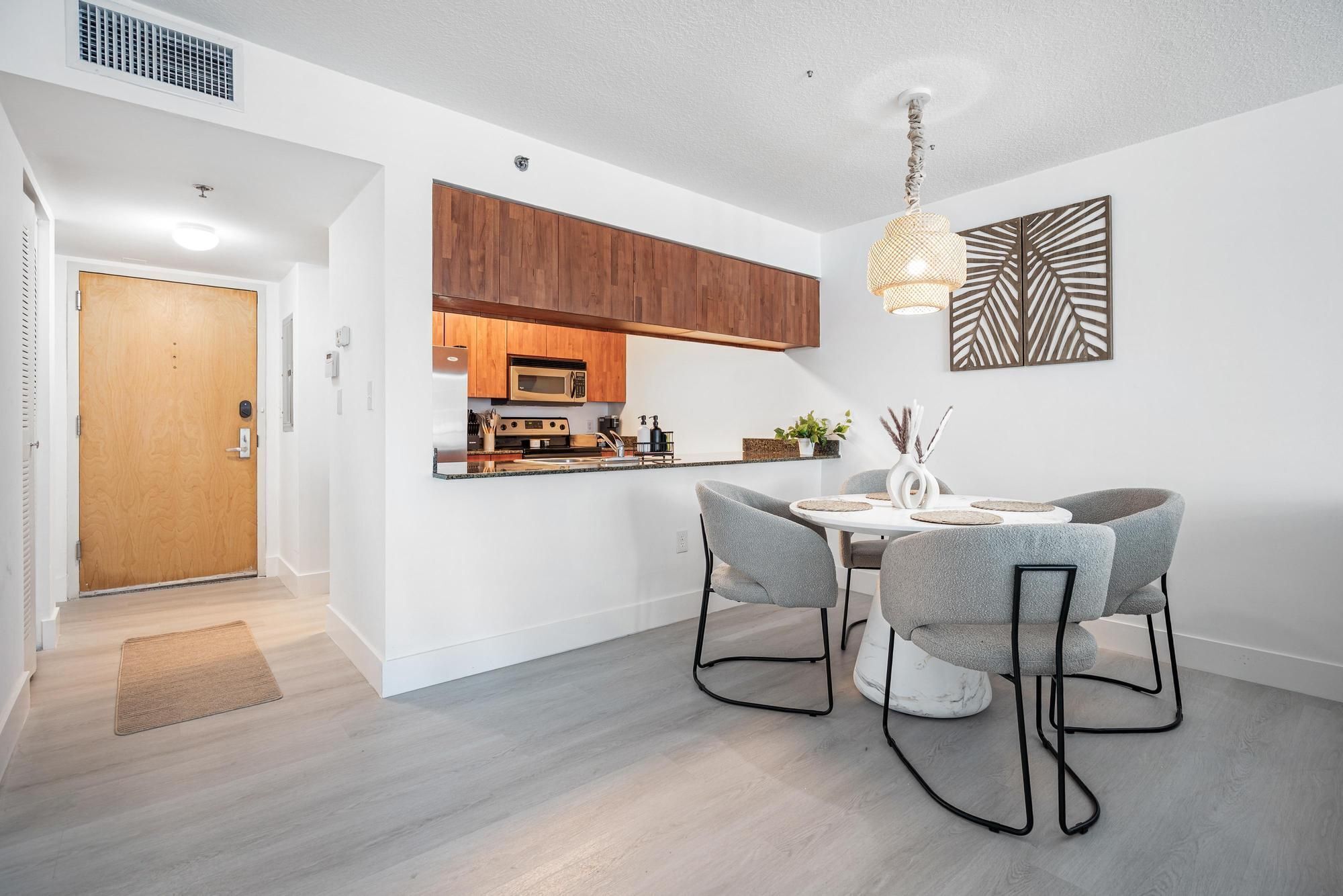 A modern kitchen with wooden cabinets, a microwave, and a dining area with grey chairs and a white table.