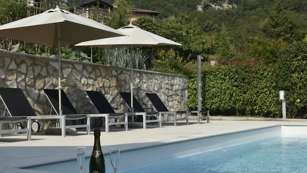 A poolside area with lounge chairs, umbrellas, and a bottle of champagne. - A 5 minuti dal Lago di Tenno, spaziosa villa con piscina vista Lago di Garda (Trentino-Alto Adige)