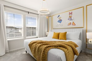 Ein Hotelzimmer mit einem großen Bett, einem Fenster mit Jalousien, einer Kristallleuchter und zwei an der Wand befestigten Illustrationen von Cartoon-Enten.