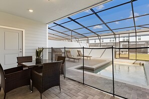 Eine überdachte Terrasse mit Glasveranda, Sitzgelegenheit im Freien und einem Pool.