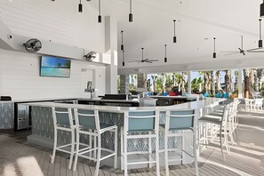 Eine moderne Bar mit weißen Barhocker, einer großen Insel-Theke und Pendelleuchten.