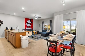 Ein modernes Wohnzimmer mit einem großen Fenster, einem Essbereich mit roten Stühlen, einer Küche mit Holzschränken und einem Wandbild mit Mickey Mouse.