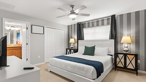 Une chambre d’hôtel avec un lit, des tables de chevet, un ventilateur de plafond et une fenêtre avec des rideaux.