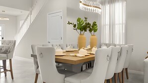 Une salle à manger moderne avec une table rectangulaire, des chaises blanches et deux grands vases ornés de plantes.