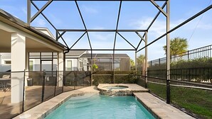 Une piscine avec un jacuzzi, entourée d’un patio couvert d’où l’on peut admirer une maison en arrière-plan.