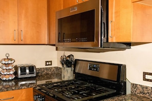 A kitchen with wooden cabinets, a stainless steel microwave, a toaster, and a gas stove. - Fair and Walker - Unit 25 (Atlanta)