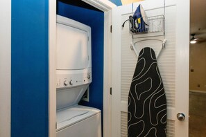 Ein Waschraum mit einer weißen Waschmaschine und einem Trockner, einer blauen Wand und einer Tür, an der ein blau-weiß gemustertes Handtuch auf einem Wäscheständer hängt.