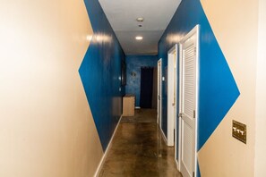 A hallway with blue walls and a brown floor, leading to a door with a white shutter. - Fair and Walker - Unit 25 (Atlanta)