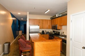 Eine kleine Küche mit Holdekor-Schränken, einem Edelstahlkühlschrank, einer Mikrowelle und einem Herd. Es gibt eine kleine Sitzecke mit zwei Stühlen.