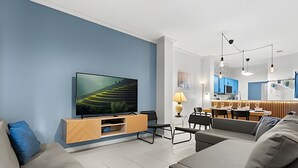 Ein modernes Wohnzimmer mit Flachbildfernseher, einer Holz-Unterhaltungsecke, einer Couch und einem Essbereich mit Tisch und Stühlen.