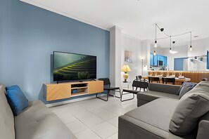 A modern living room with a flat-screen TV, a wooden entertainment unit, a sofa, and a dining area with a table and chairs. - 3 Bd / 2,5 Ba / Sleeps 08/ Terra Verde Resort (Kissimmee)