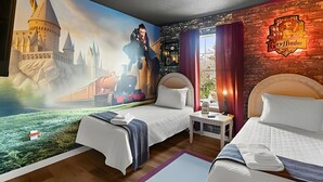 Ein Hotelzimmer mit zwei Betten, einem Wandgemälde eines Schlosses, einem Schild mit 'Hogwarts' und einem Fenster mit Vorhängen.
