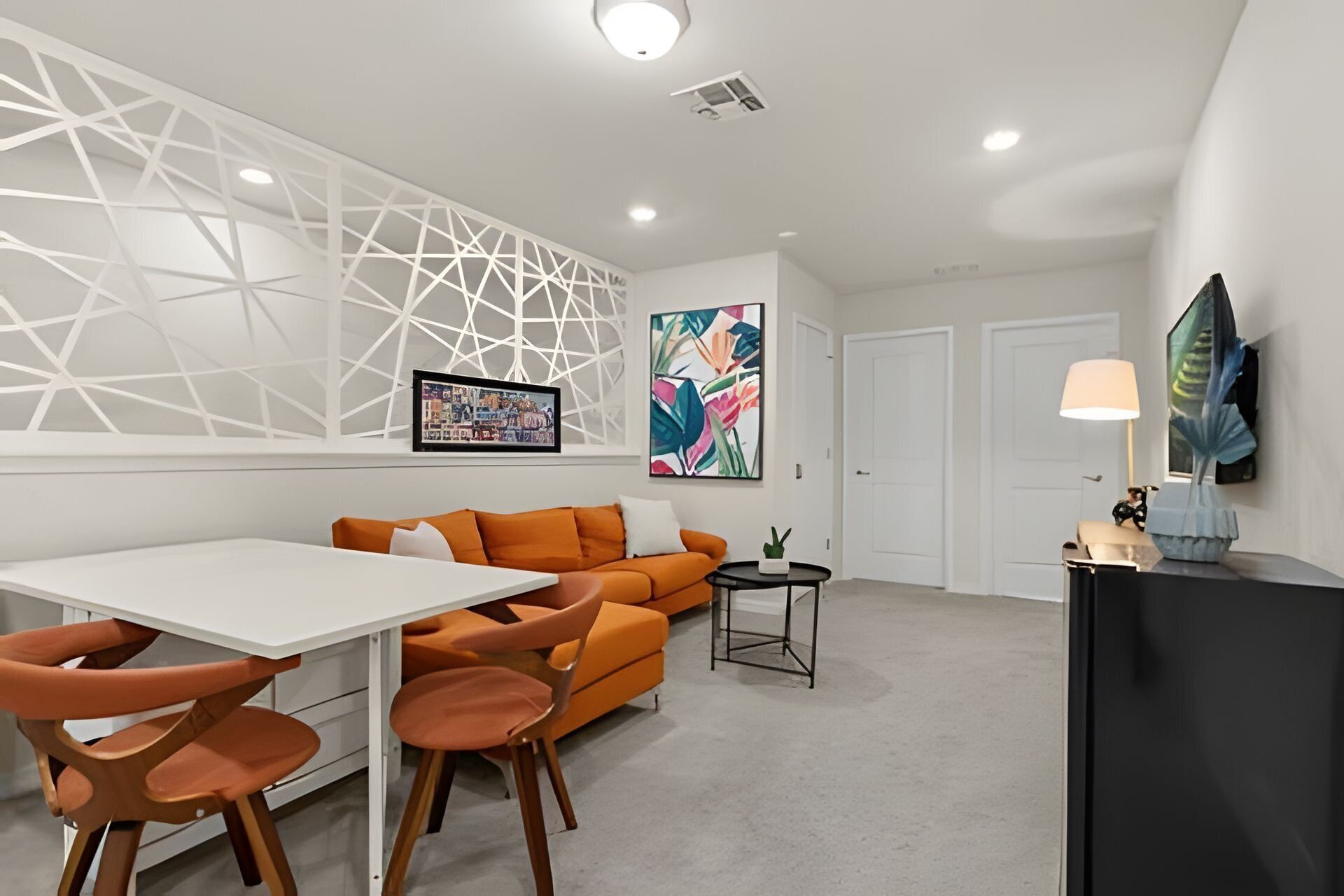 A modern living room with a white dining table, orange sofa, and a black side table.