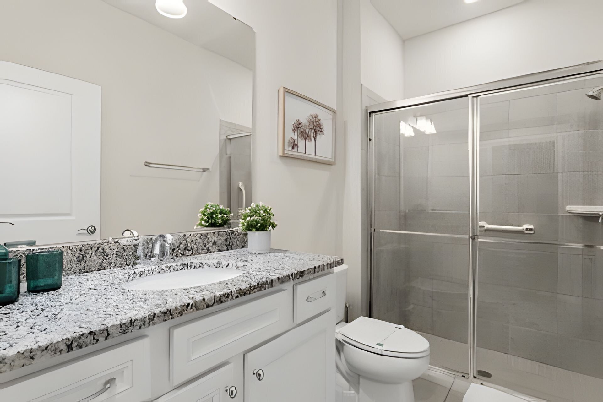 A modern bathroom with a granite countertop, a white toilet, and a glass-enclosed shower.