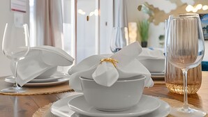 Een gedekte tafel met witte servies, een schaal met een servetje, en een glas water.