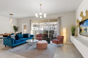 Ein modernes Wohnzimmer mit einem blauen Sofa, einem runden Couchtisch und einem roten Sessel. Ein großes Fenster bietet Blick auf eine Stadtansicht.