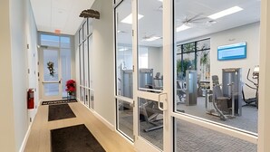 Een moderne kantoorruimte met glazen scheidingswanden, een receptiegedeelte met een plant en fitnessapparatuur.