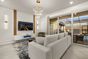 Ein modernes Wohnzimmer mit einer großen Couch, einem Flachbildfernseher und einem Essbereich mit Tisch und Stühlen.